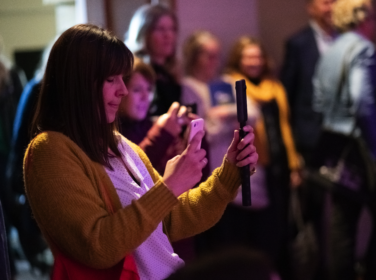 Claire holding a 360 camera in a busy room of people. 
